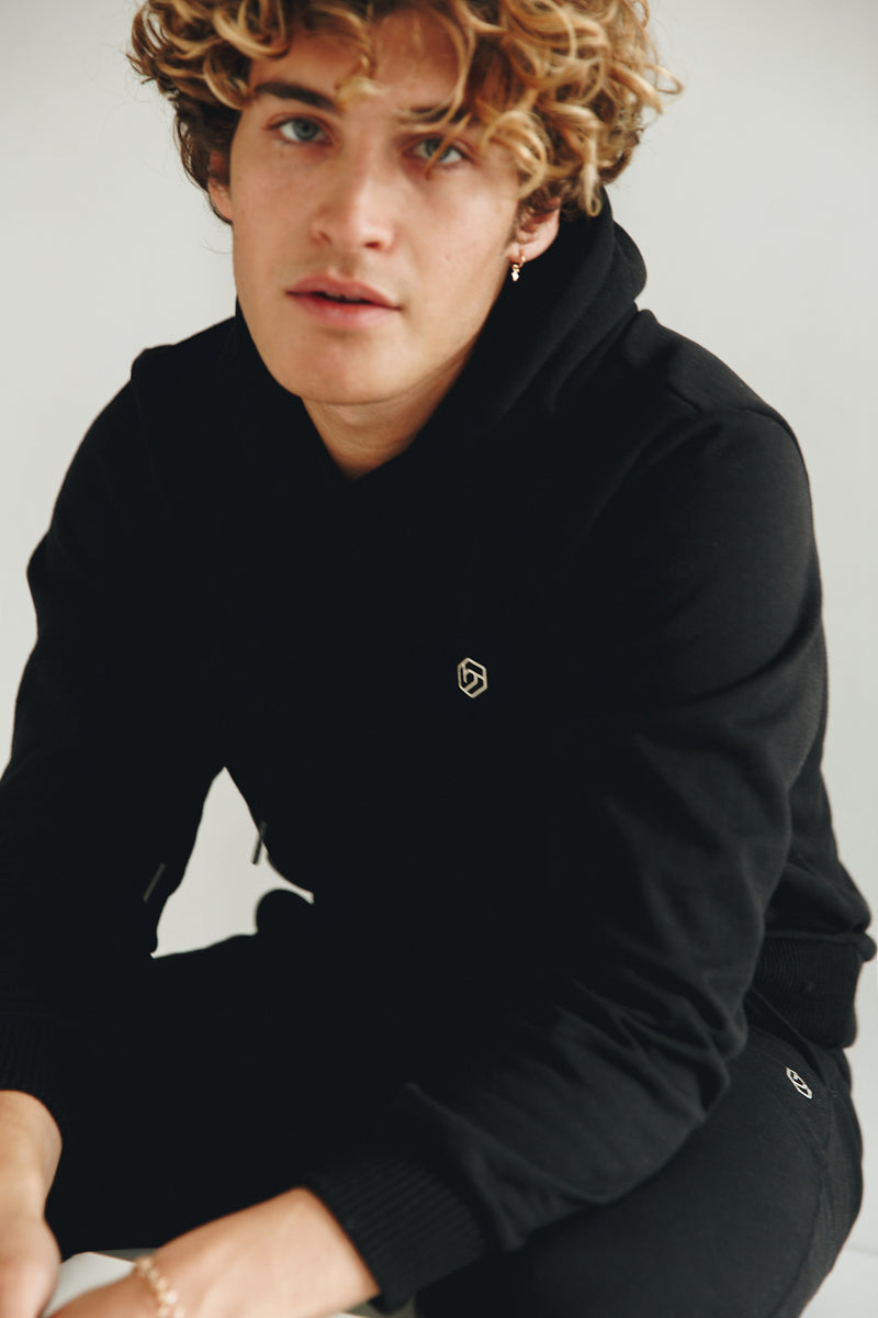 Model wearing Hexed Fashion black sustainable unisex hoodie with logo print on chest